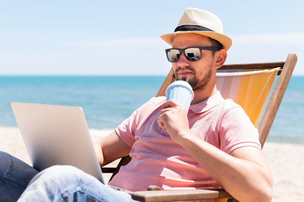 homme buvant sur la plage et travaillant sur son ordinateur portable