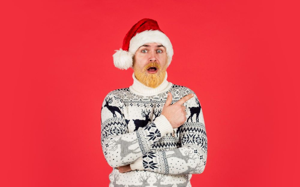new year party is here christmas shopping time mature male knitted xmas sweater brutal man hate winter holidays surprised man santa hat bearded hipster dyed hair red background